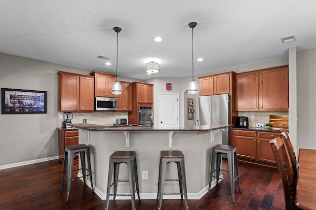 kitchen featuring appliances with stainless steel finishes, a kitchen bar, brown cabinets, dark wood finished floors, and recessed lighting
