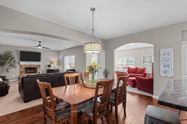 dining space featuring a ceiling fan, dark wood-style flooring, plenty of natural light, and a fireplace