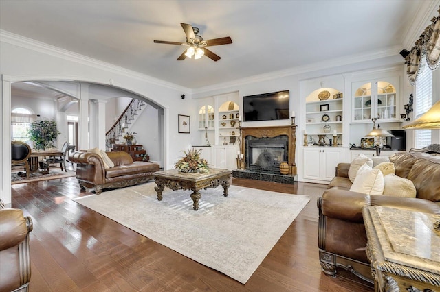 living room with built in shelves, ceiling fan, decorative columns, a fireplace, and ornamental molding