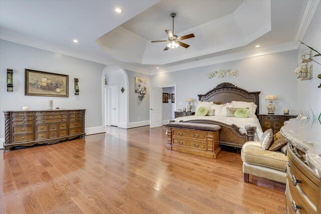 bedroom with light wood-type flooring, a tray ceiling, ceiling fan, and crown molding