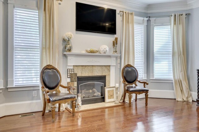 living area with a tile fireplace, hardwood / wood-style floors, and ornamental molding