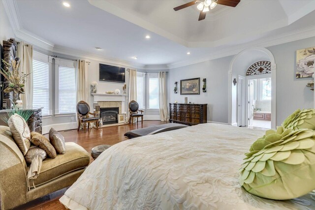 bedroom featuring a fireplace, wood-type flooring, a tray ceiling, and ceiling fan