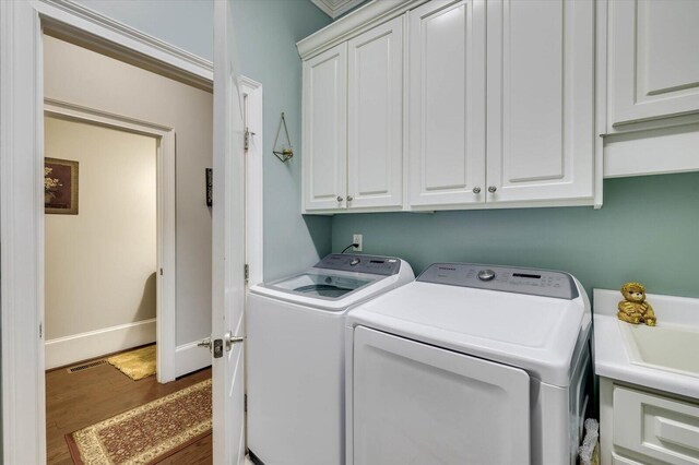 laundry area featuring washing machine and dryer, cabinets, and hardwood / wood-style flooring