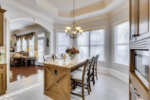 tiled dining space with a notable chandelier, crown molding, and a tray ceiling