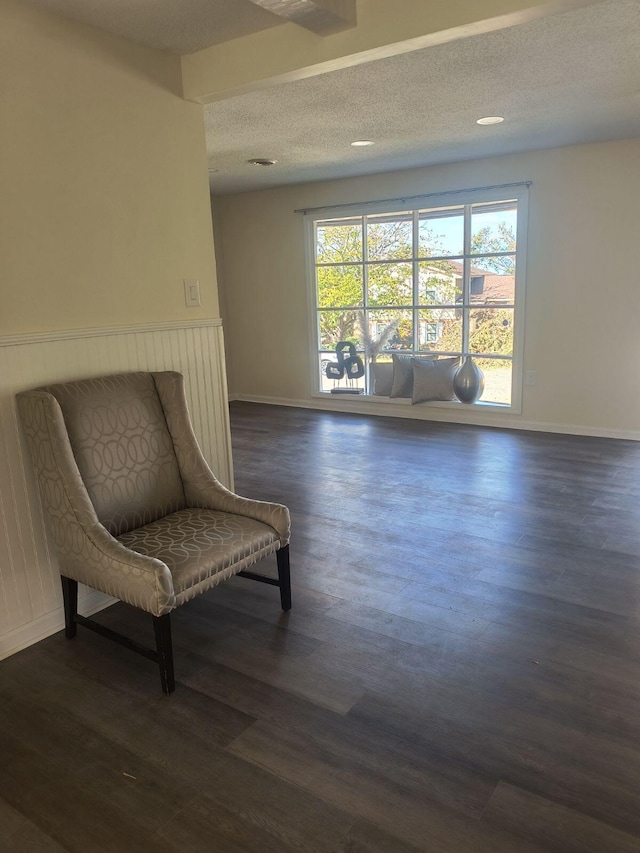 living area featuring a textured ceiling, beam ceiling, and dark wood-type flooring