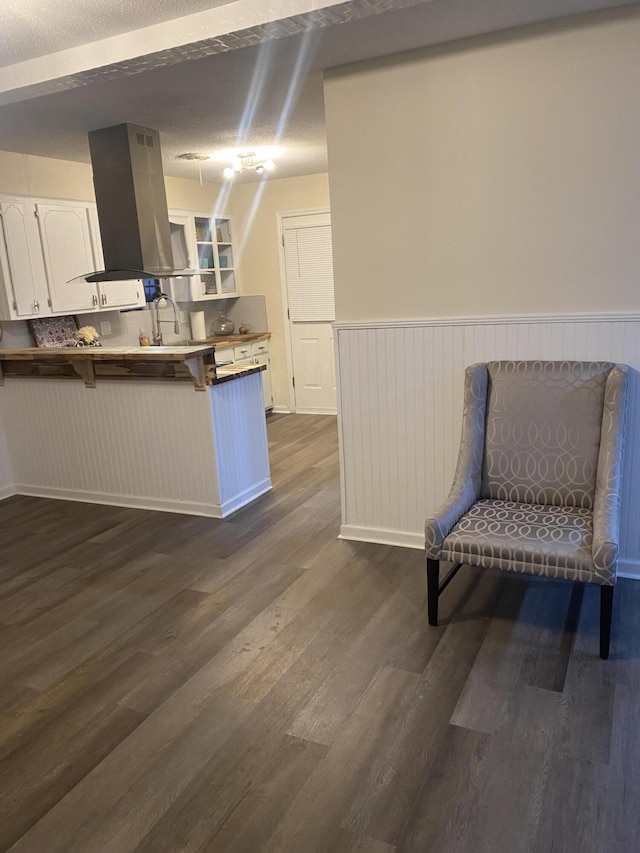 kitchen featuring white cabinetry, dark hardwood / wood-style floors, island exhaust hood, kitchen peninsula, and a kitchen bar