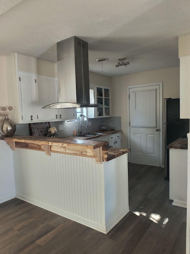 kitchen featuring kitchen peninsula, island range hood, white cabinetry, and tasteful backsplash