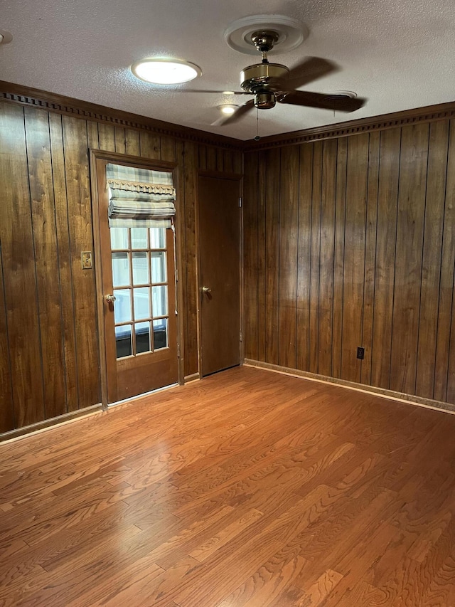 spare room with ceiling fan, light wood-type flooring, wood walls, and a textured ceiling