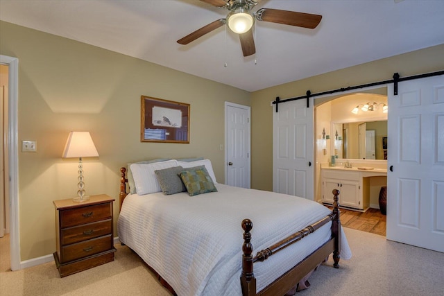 bedroom with light carpet, a barn door, ceiling fan, ensuite bath, and sink