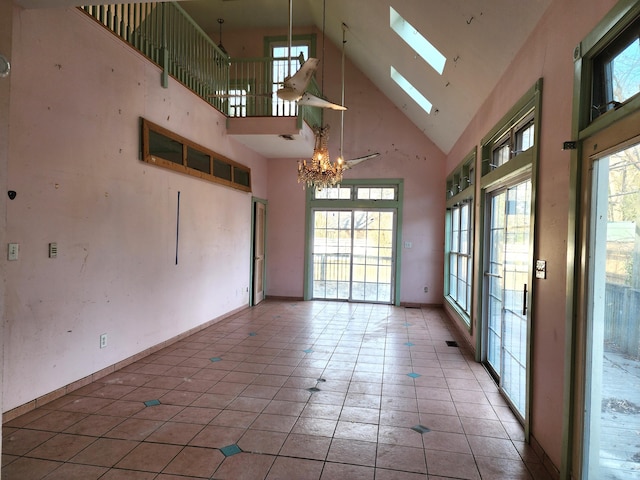 spare room featuring a high ceiling, tile patterned floors, a chandelier, and a skylight