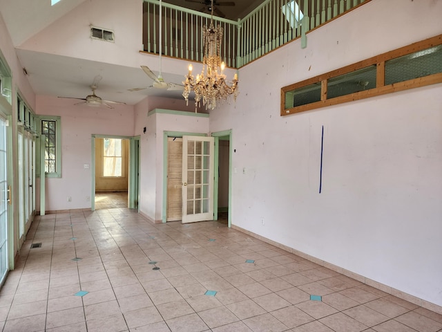 spare room with light tile patterned floors, ceiling fan with notable chandelier, and a towering ceiling