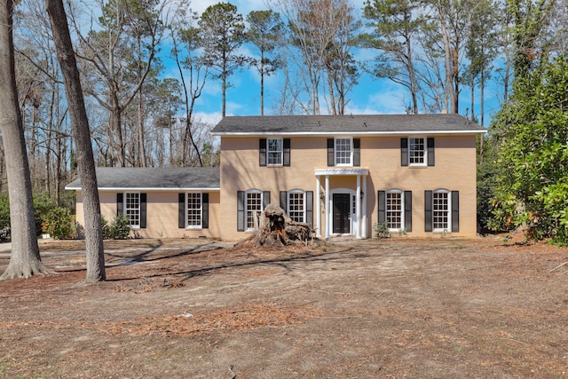 colonial house featuring roof with shingles and stucco siding