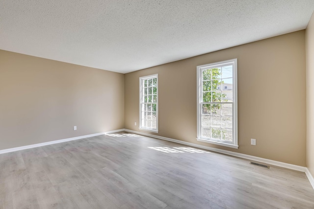 empty room with visible vents, baseboards, a textured ceiling, and wood finished floors