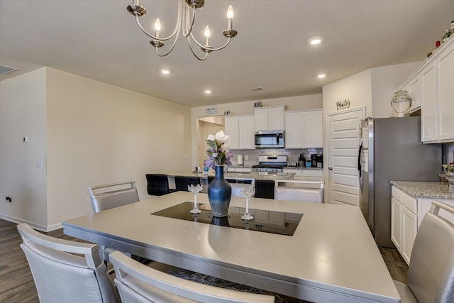 kitchen with appliances with stainless steel finishes, tasteful backsplash, pendant lighting, an inviting chandelier, and white cabinets