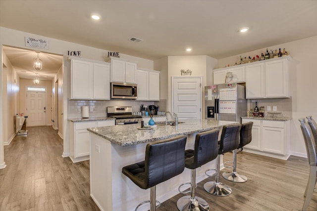 kitchen with appliances with stainless steel finishes, white cabinetry, and an island with sink