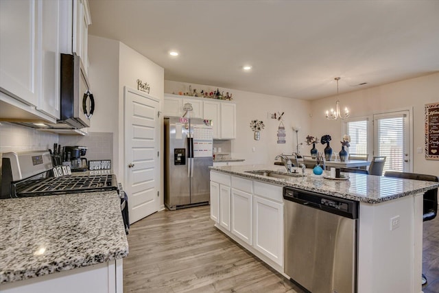 kitchen featuring hanging light fixtures, stainless steel appliances, white cabinetry, and a kitchen island with sink