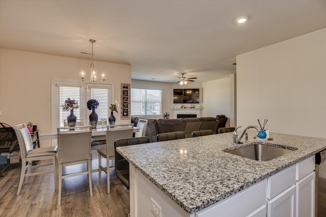 kitchen with ceiling fan with notable chandelier, a kitchen island with sink, sink, pendant lighting, and white cabinets