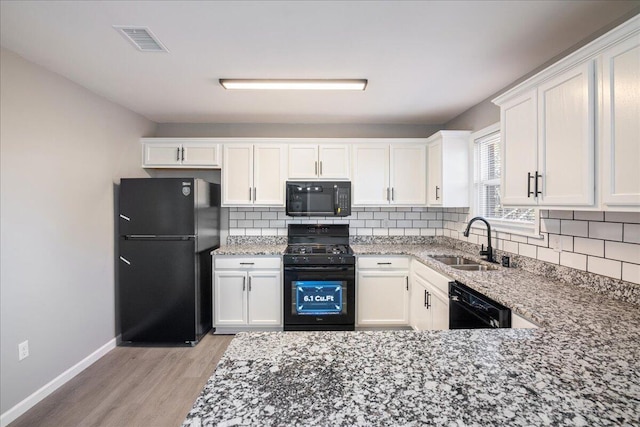 kitchen with white cabinetry, sink, light stone counters, and black appliances