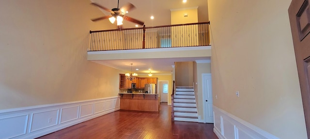 interior space with ceiling fan with notable chandelier, ornamental molding, dark wood-type flooring, and a high ceiling