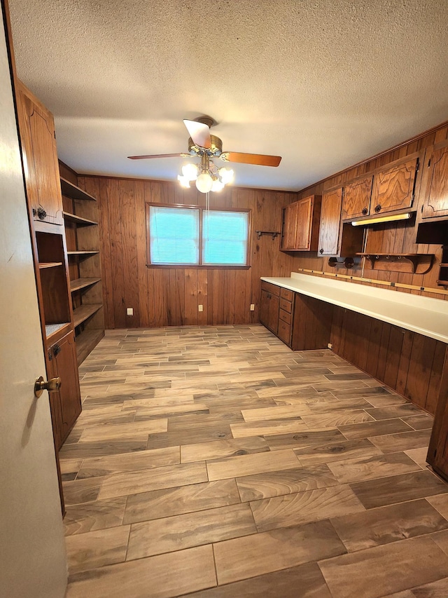 2023 Pisgah Rd, North Augusta, SC 29841 - kitchen featuring ceiling fan, wood walls, brown cabinetry, light wood-type flooring, and a textured ceiling