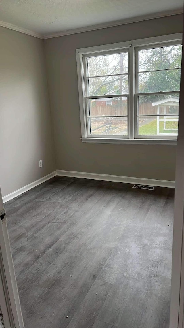 unfurnished room with a healthy amount of sunlight, crown molding, and dark wood-type flooring