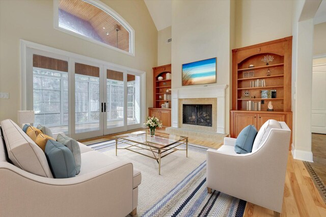 living room featuring built in shelves, light hardwood / wood-style flooring, a healthy amount of sunlight, and a high ceiling