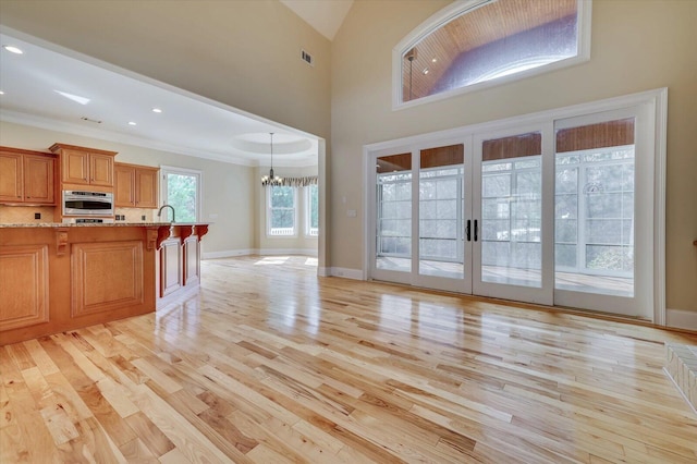 unfurnished living room featuring a notable chandelier, light hardwood / wood-style floors, crown molding, and french doors