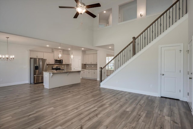 unfurnished living room with a towering ceiling, light hardwood / wood-style floors, and ceiling fan with notable chandelier