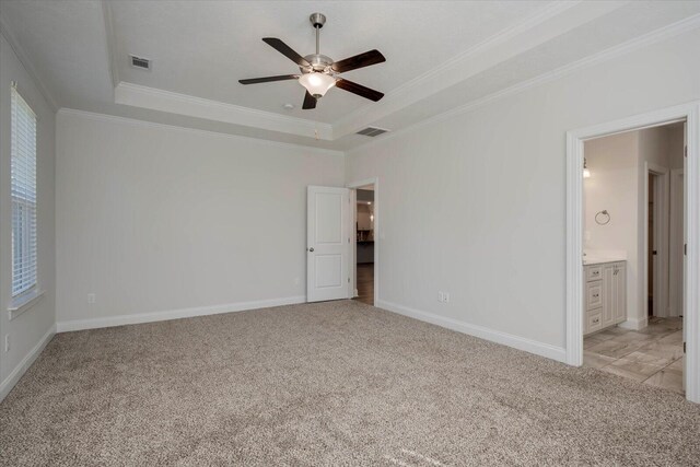 unfurnished bedroom featuring a raised ceiling, crown molding, ensuite bath, ceiling fan, and light colored carpet