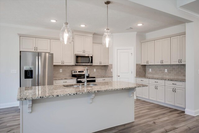 kitchen featuring light stone countertops, appliances with stainless steel finishes, sink, a center island with sink, and hanging light fixtures