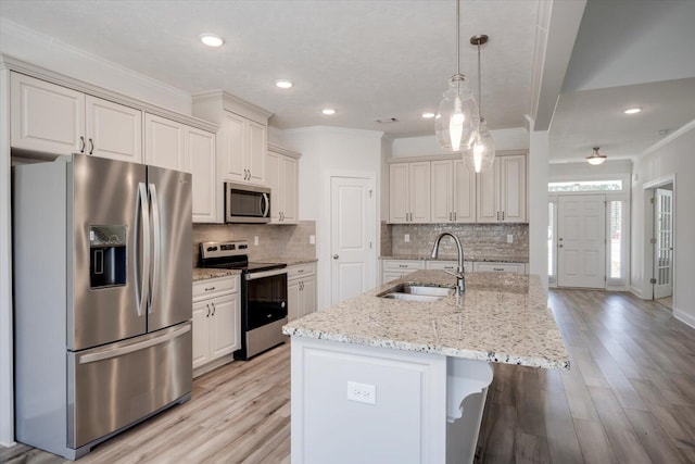 kitchen with light stone countertops, appliances with stainless steel finishes, a kitchen island with sink, sink, and decorative light fixtures