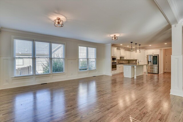 unfurnished living room featuring hardwood / wood-style flooring, sink, and crown molding