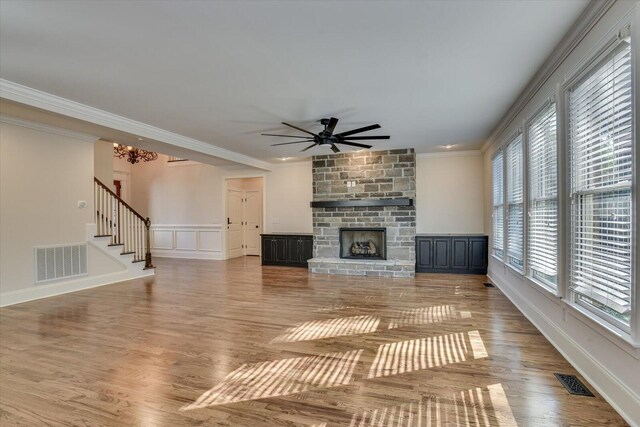 unfurnished living room featuring hardwood / wood-style floors, ceiling fan with notable chandelier, a stone fireplace, and crown molding