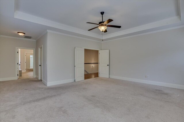 unfurnished bedroom with a raised ceiling, ceiling fan, light carpet, and ornamental molding