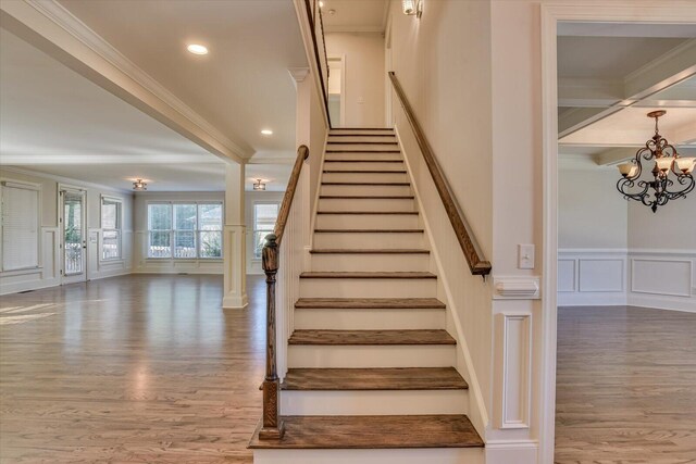 stairway featuring hardwood / wood-style floors, an inviting chandelier, and ornamental molding