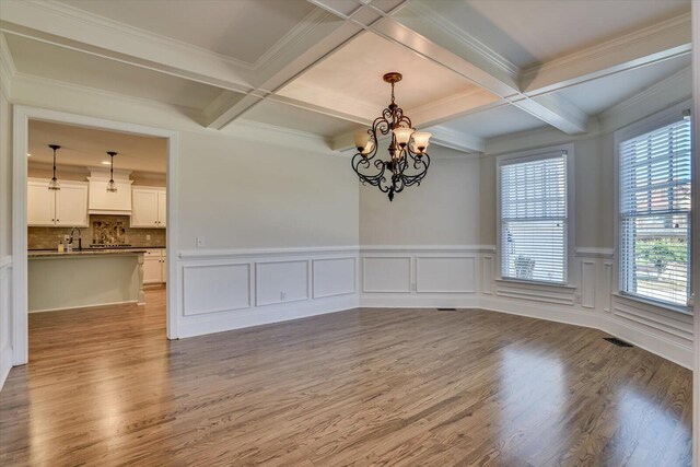 spare room featuring beam ceiling, light hardwood / wood-style floors, coffered ceiling, and a notable chandelier