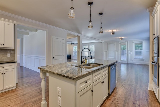 kitchen featuring appliances with stainless steel finishes, dark stone counters, a kitchen island with sink, sink, and white cabinets