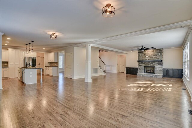 unfurnished living room featuring ornamental molding, ceiling fan, sink, light hardwood / wood-style floors, and a stone fireplace