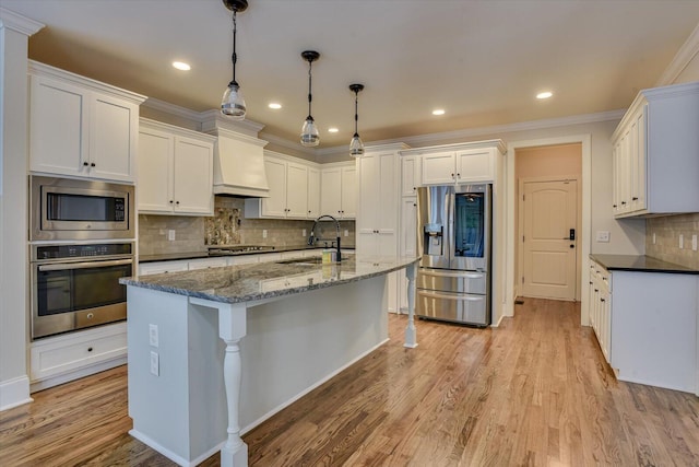 kitchen with white cabinets, sink, appliances with stainless steel finishes, decorative light fixtures, and custom range hood