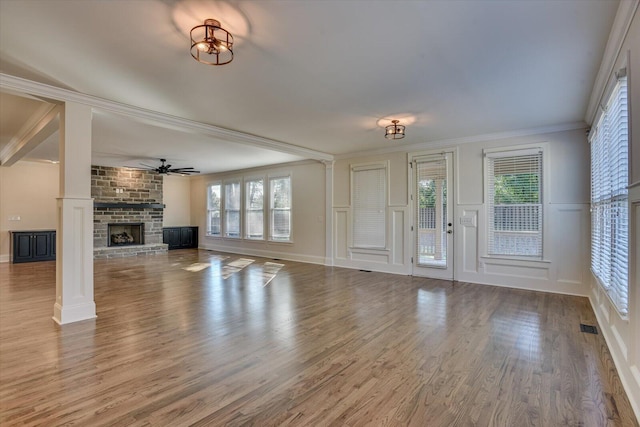 unfurnished living room with decorative columns, ornamental molding, ceiling fan, wood-type flooring, and a fireplace