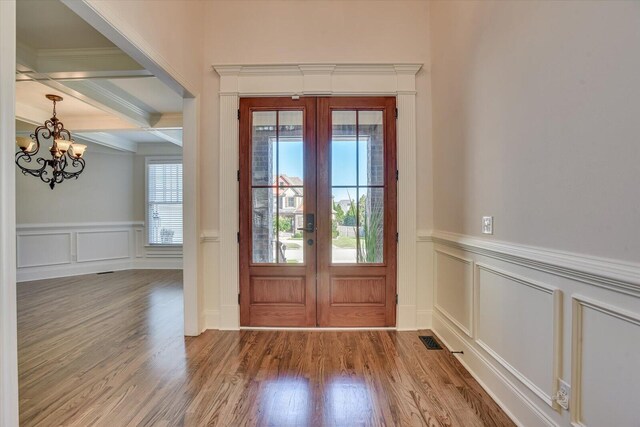 foyer entrance with beam ceiling, french doors, wood-type flooring, a chandelier, and ornamental molding