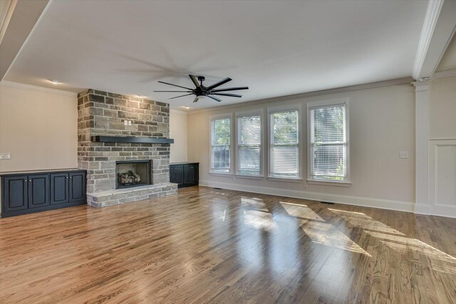 unfurnished living room featuring a stone fireplace, ceiling fan, and crown molding