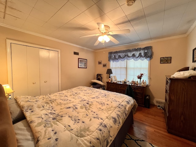 bedroom featuring wood finished floors, a closet, crown molding, baseboards, and ceiling fan