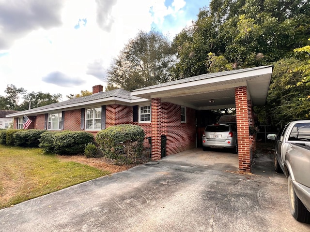 view of side of property featuring driveway, a yard, a chimney, a carport, and brick siding