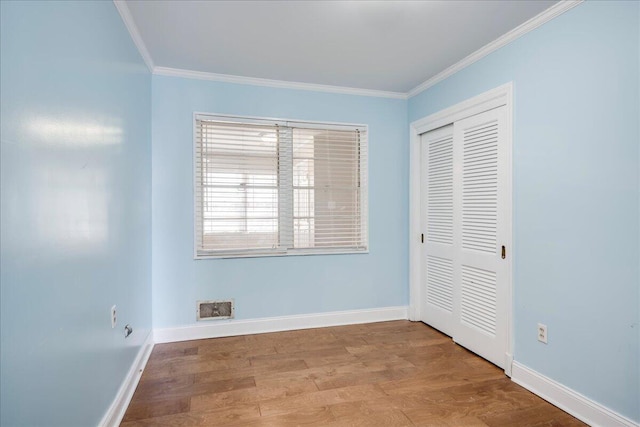 unfurnished bedroom featuring ornamental molding, wood finished floors, visible vents, and baseboards