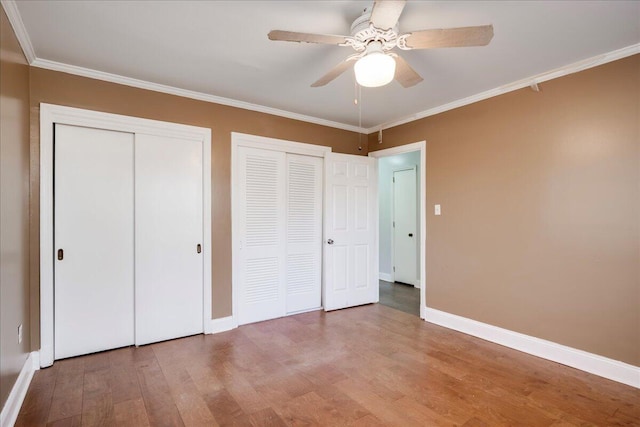 unfurnished bedroom with baseboards, ceiling fan, ornamental molding, wood finished floors, and multiple closets