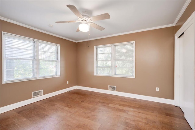 spare room with baseboards, light wood finished floors, visible vents, and crown molding