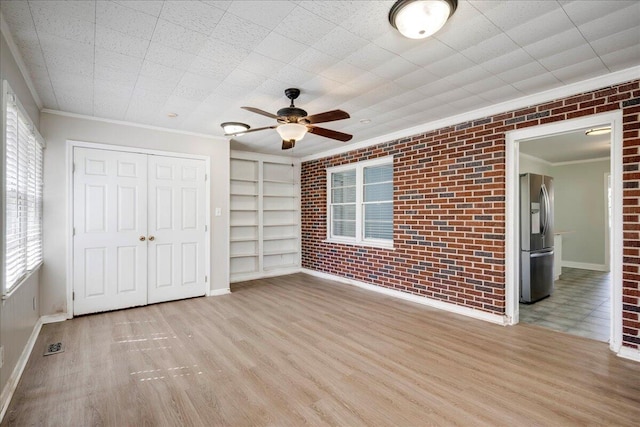 unfurnished bedroom with stainless steel fridge with ice dispenser, brick wall, wood finished floors, crown molding, and a closet