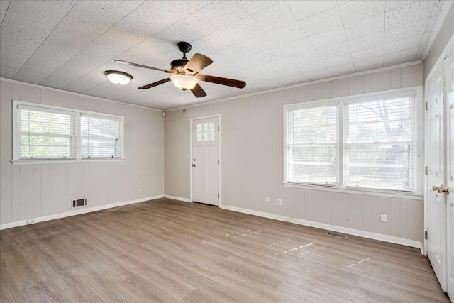 empty room with light wood-style floors, visible vents, and crown molding