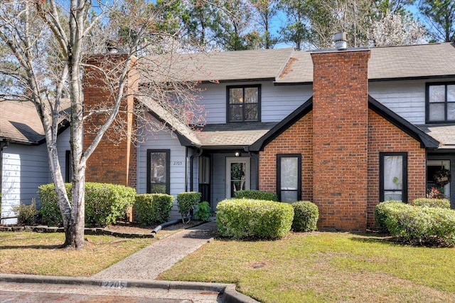 view of front facade with brick siding, a chimney, a front lawn, and roof with shingles